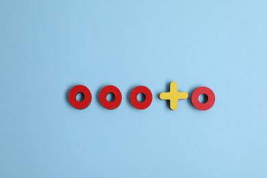 Choice concept. Red wooden circles and yellow cross on light blue background, flat lay