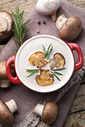 Delicious homemade mushroom soup in ceramic pot and fresh ingredients on wooden table, flat lay