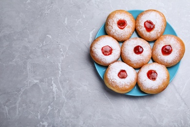 Photo of Hanukkah doughnuts with jelly and sugar powder on grey marble table, top view. Space for text