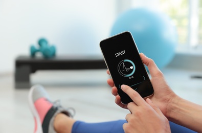 Young woman using fitness app on smartphone indoors, closeup. Space for text
