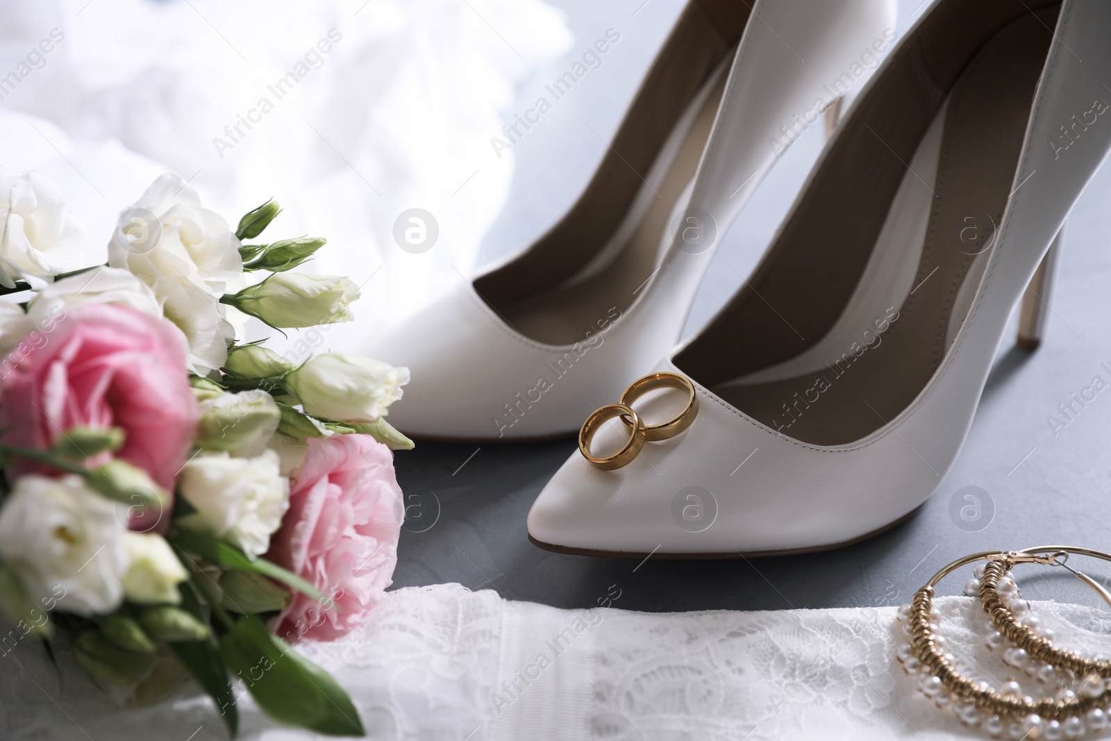 Photo of Composition with wedding dress, white high heel shoes and rings on grey background