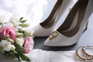 Photo of Composition with wedding dress, white high heel shoes and rings on grey background