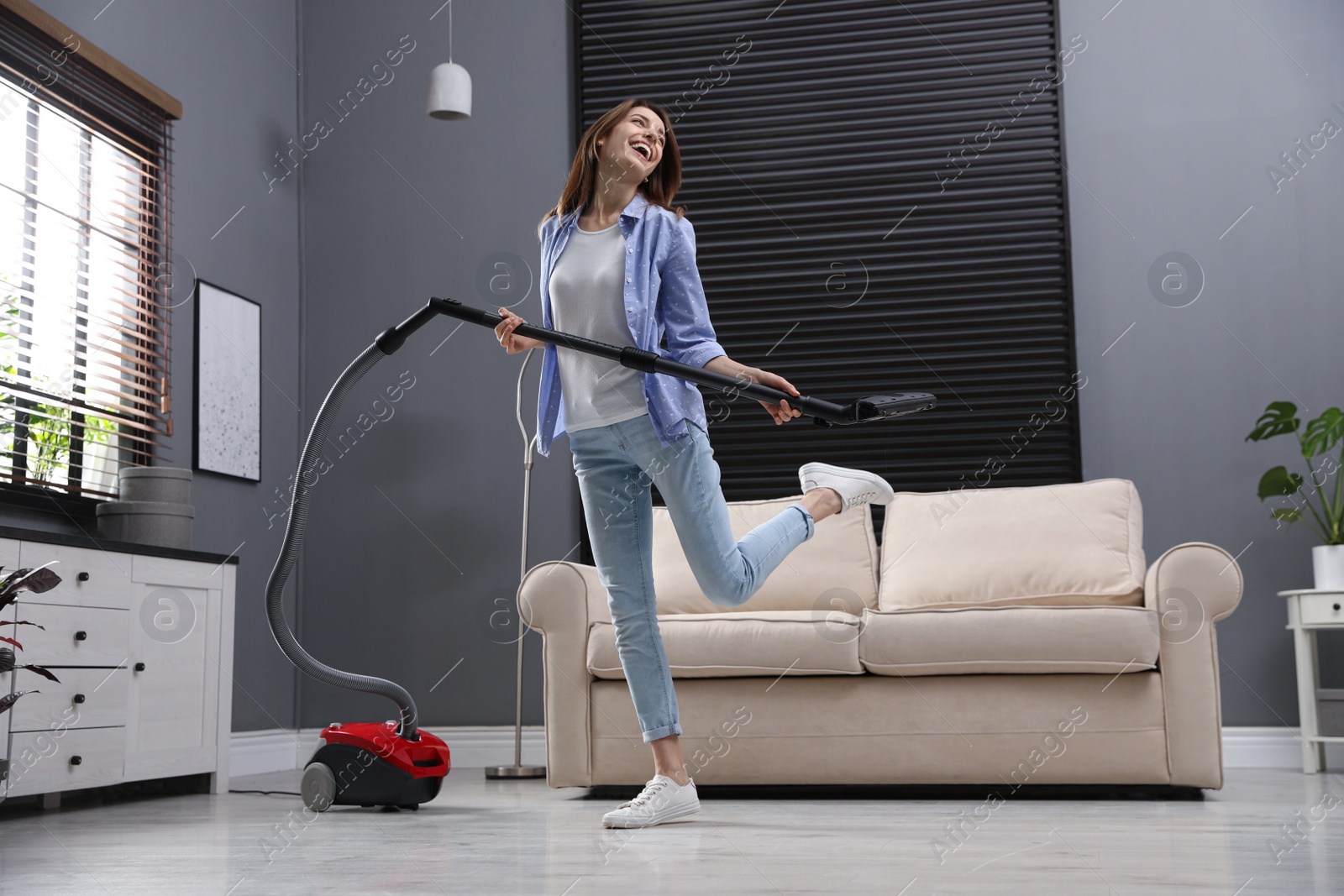 Photo of Young woman having fun while vacuuming at home