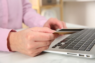 Photo of Online payment. Woman using credit card and laptop at white marble table indoors, closeup