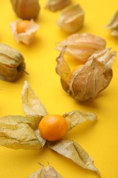 Photo of Ripe physalis fruits with calyxes on yellow background, closeup