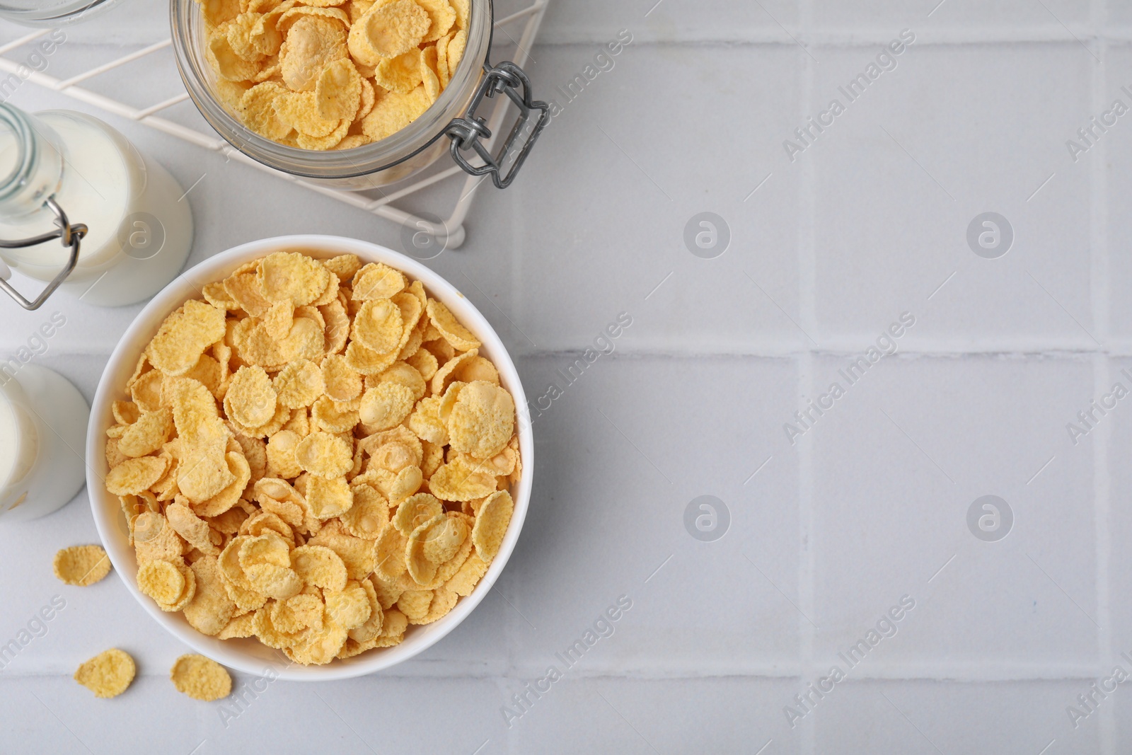 Photo of Breakfast cereal. Tasty crispy corn flakes and milk on white tiled table, flat lay. Space for text