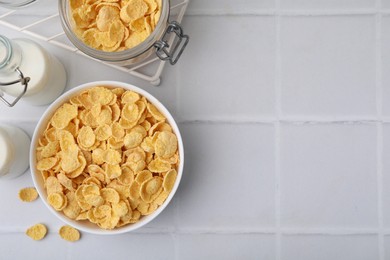 Breakfast cereal. Tasty crispy corn flakes and milk on white tiled table, flat lay. Space for text