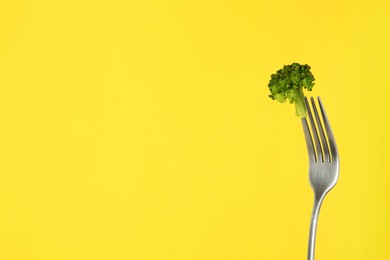 Fork with tasty broccoli on yellow background, space for text
