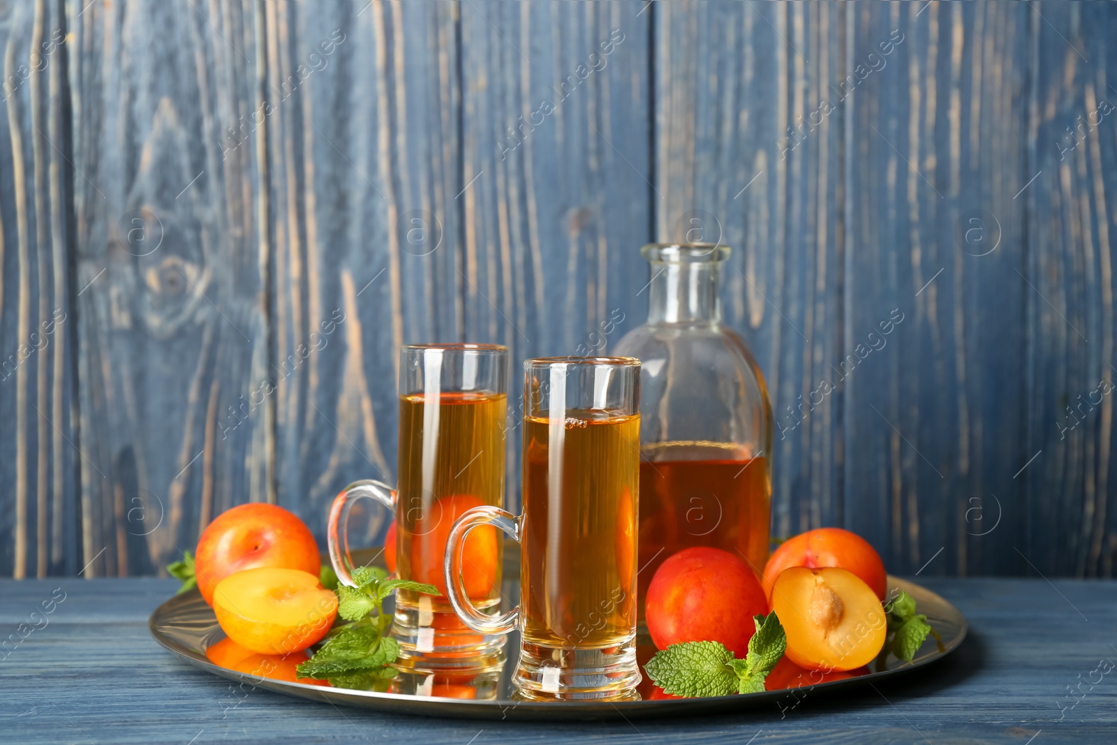 Photo of Delicious plum liquor, mint and ripe fruits on blue wooden table. Homemade strong alcoholic beverage