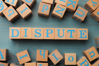 Cubes with word Dispute on light blue wooden table, flat lay