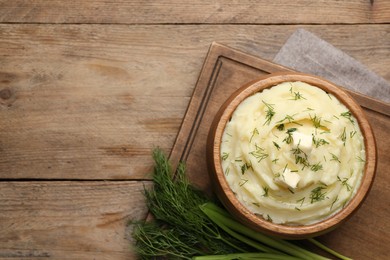 Photo of Bowl of delicious mashed potato with dill and butter on wooden table, flat lay