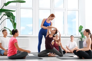 Photo of Yoga coach helping woman during group lesson indoors