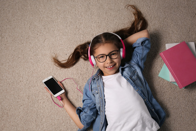 Photo of Cute little girl listening to audiobook on floor, top view