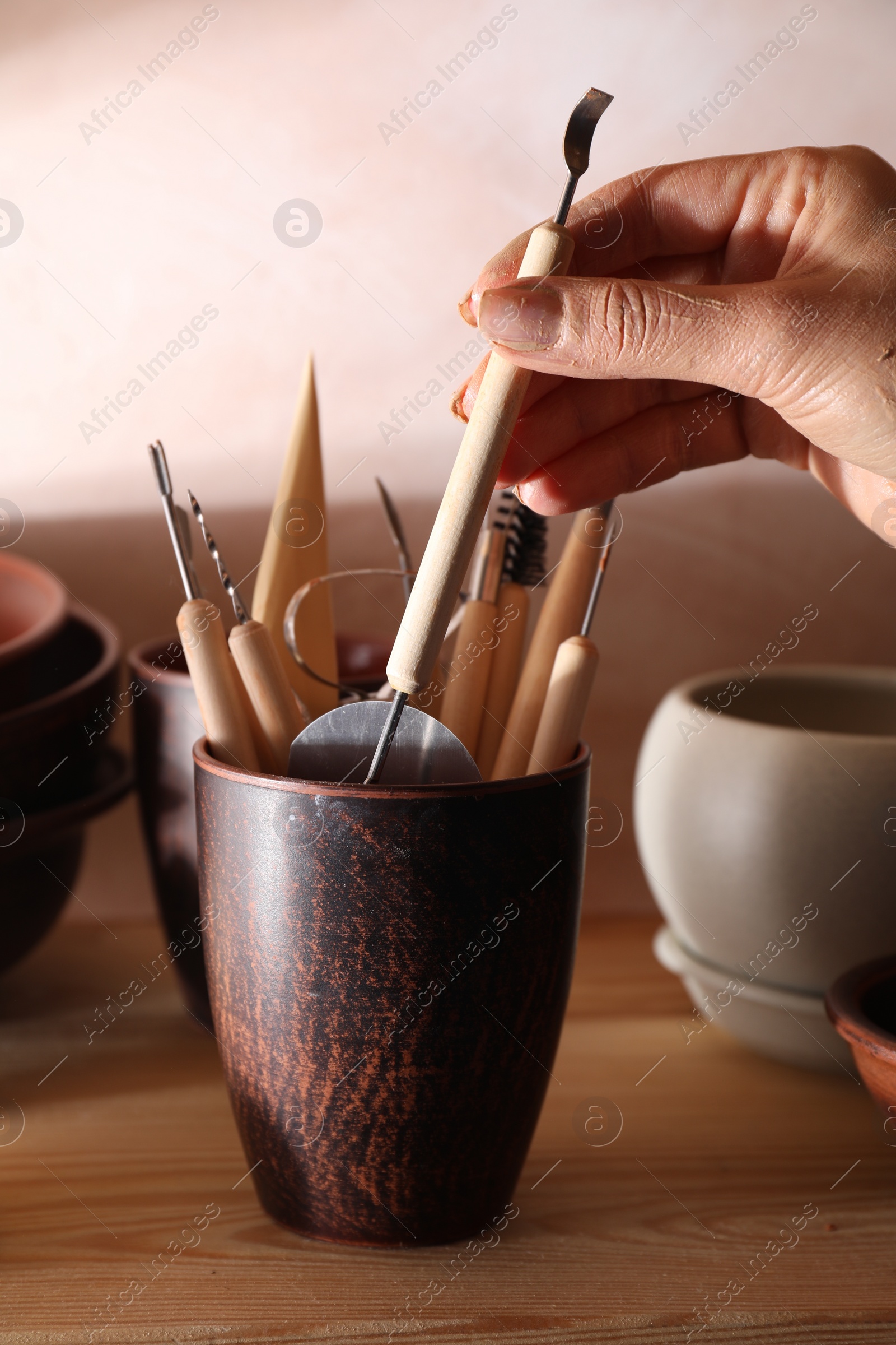 Photo of Woman taking clay crafting tool from cup in workshop, closeup