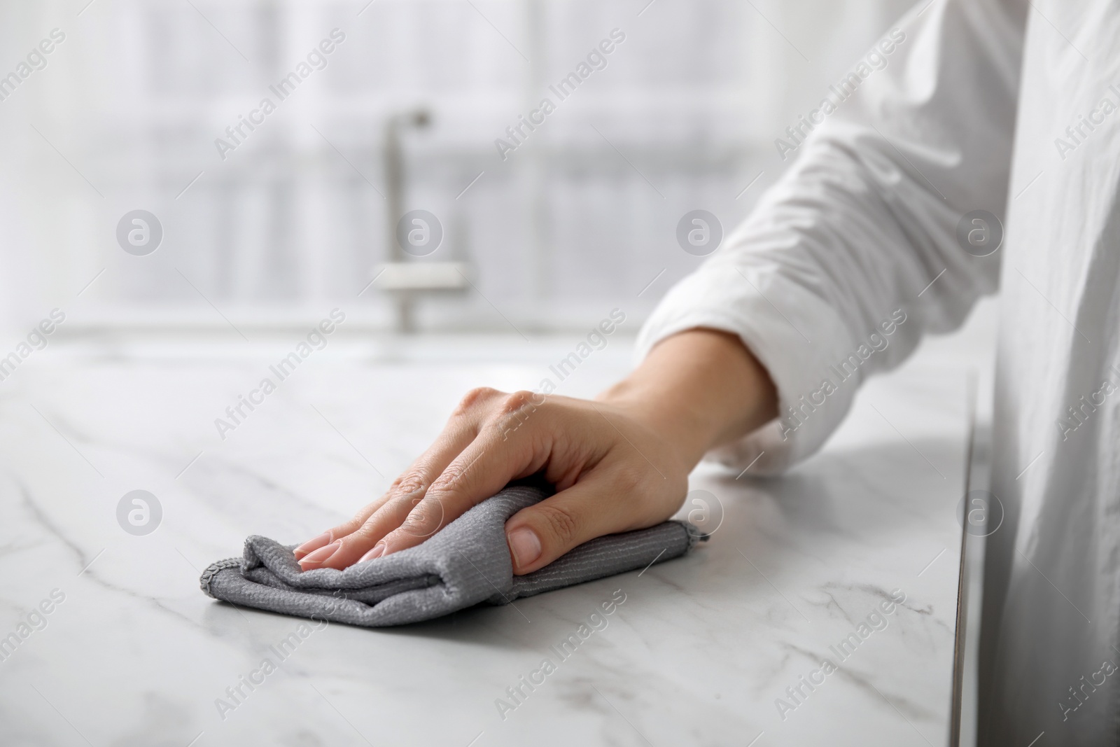 Photo of Woman wiping white marble table indoors, closeup