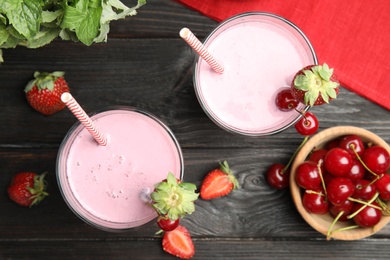 Photo of Tasty fresh milk shakes with berries on black wooden table, flat lay