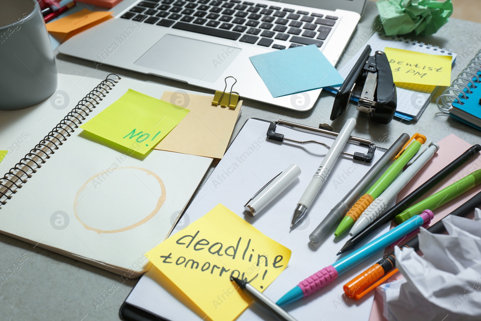 Photo of Messy table with laptop and stationery. Concept of being overwhelmed by work