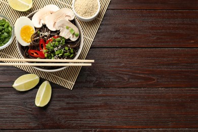 Photo of Tasty buckwheat noodles (soba) with egg and mushrooms served on wooden table, flat lay. Space for text