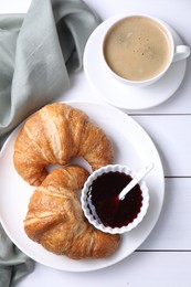 Fresh croissants, jam and coffee on white wooden table, flat lay. Tasty breakfast