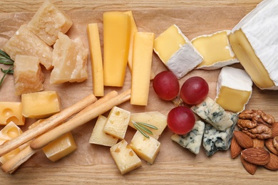 Photo of Cheese plate with grapes, grissini and nuts on wooden board, top view