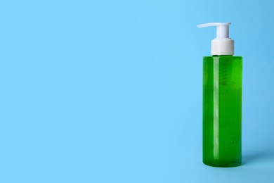 Bottle of face cleansing product on light blue background. Space for text