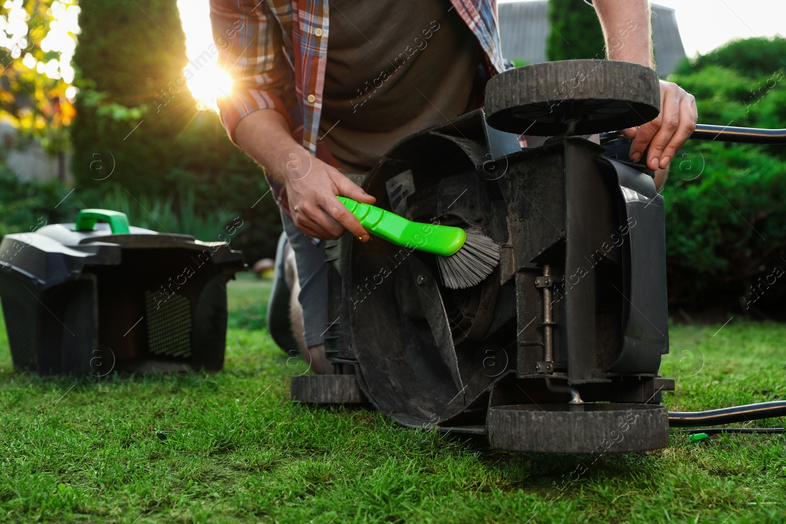 Photo of Man cleaning lawn mower with brush in garden, closeup