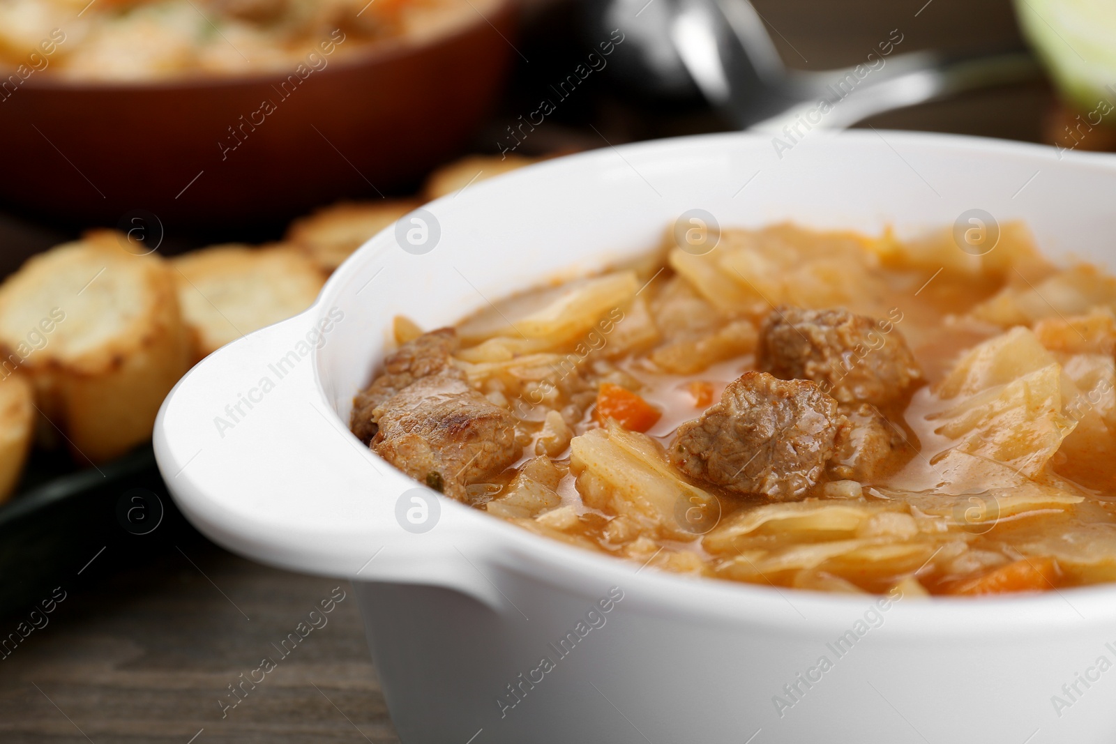 Photo of Tasty cabbage soup with meat and carrot on wooden table, closeup