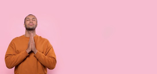 Photo of African American man with clasped hands praying to God on pink background. Space for text