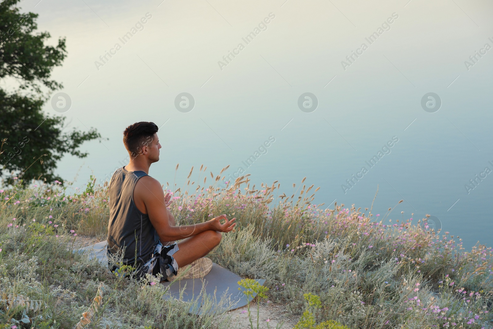 Photo of Man meditating in meadow near river. Space for text