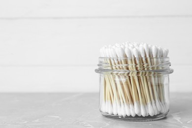 Photo of Many cotton buds in glass jar on light grey marble table, space for text