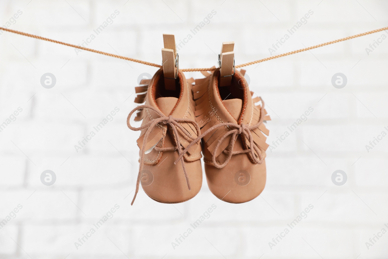 Photo of Cute baby shoes drying on washing line against white brick wall