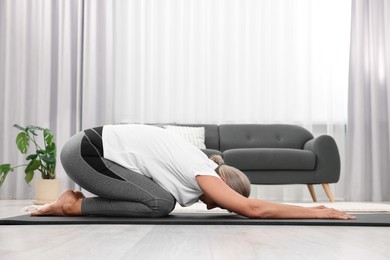 Senior woman practicing yoga on mat at home