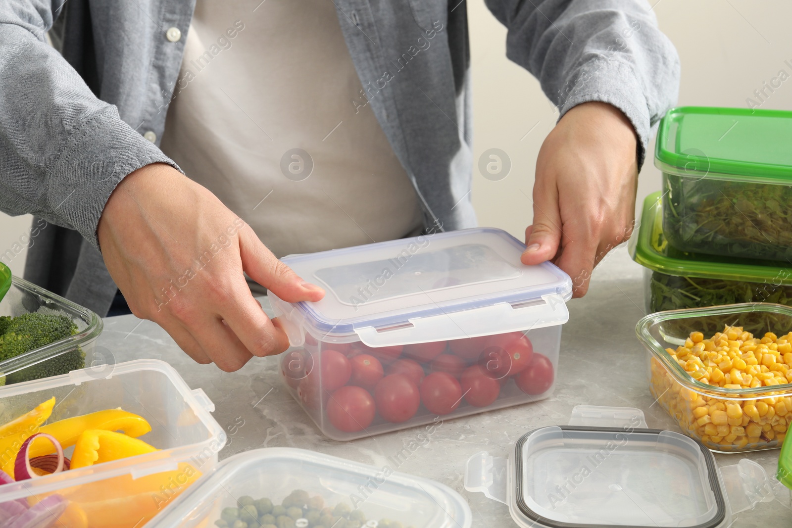 Photo of Man closing plastic container with lid at light grey marble table in kitchen, closeup. Food storage