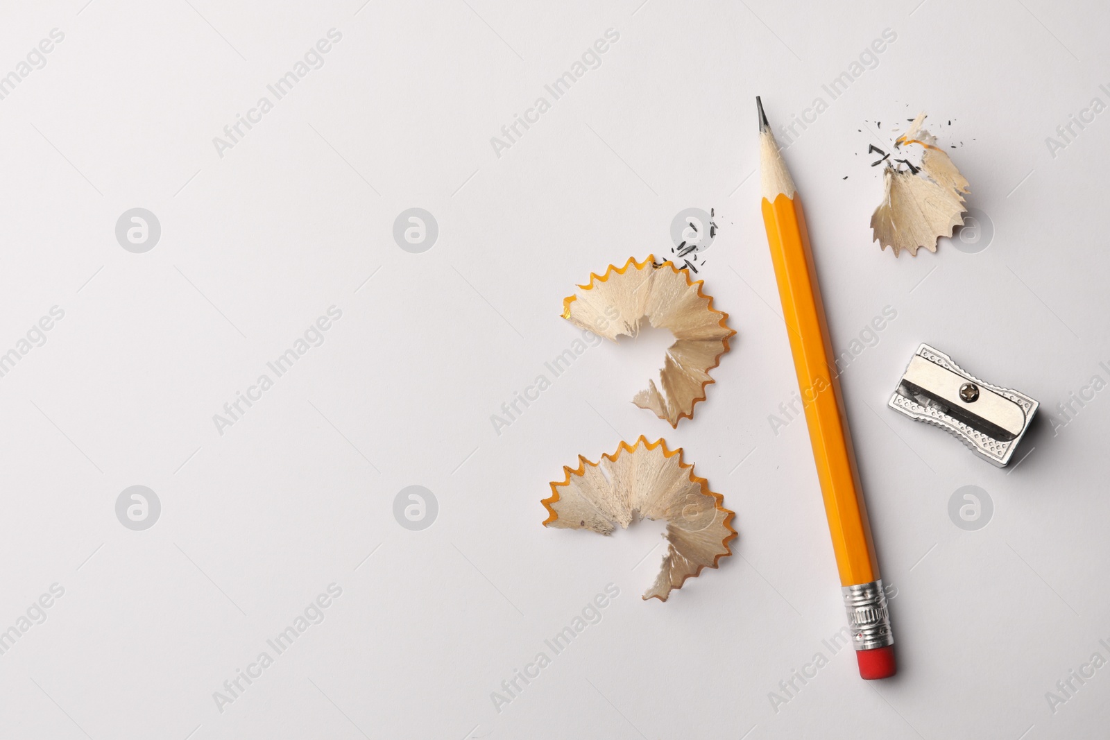 Photo of Graphite pencil, shavings and sharpener on white background, flat lay. Space for text