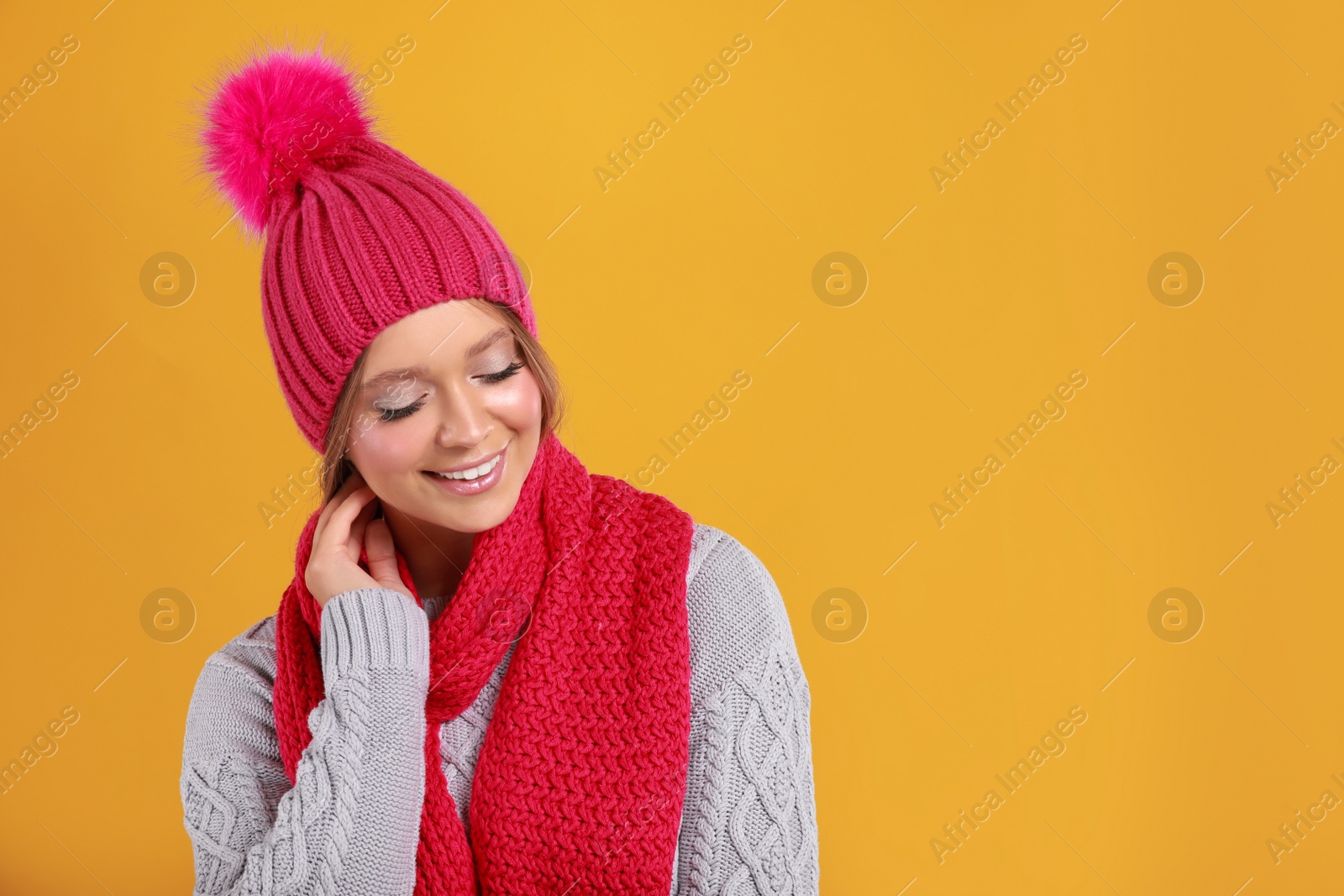 Photo of Young woman in warm sweater, scarf and hat on yellow background, space for text. Winter season