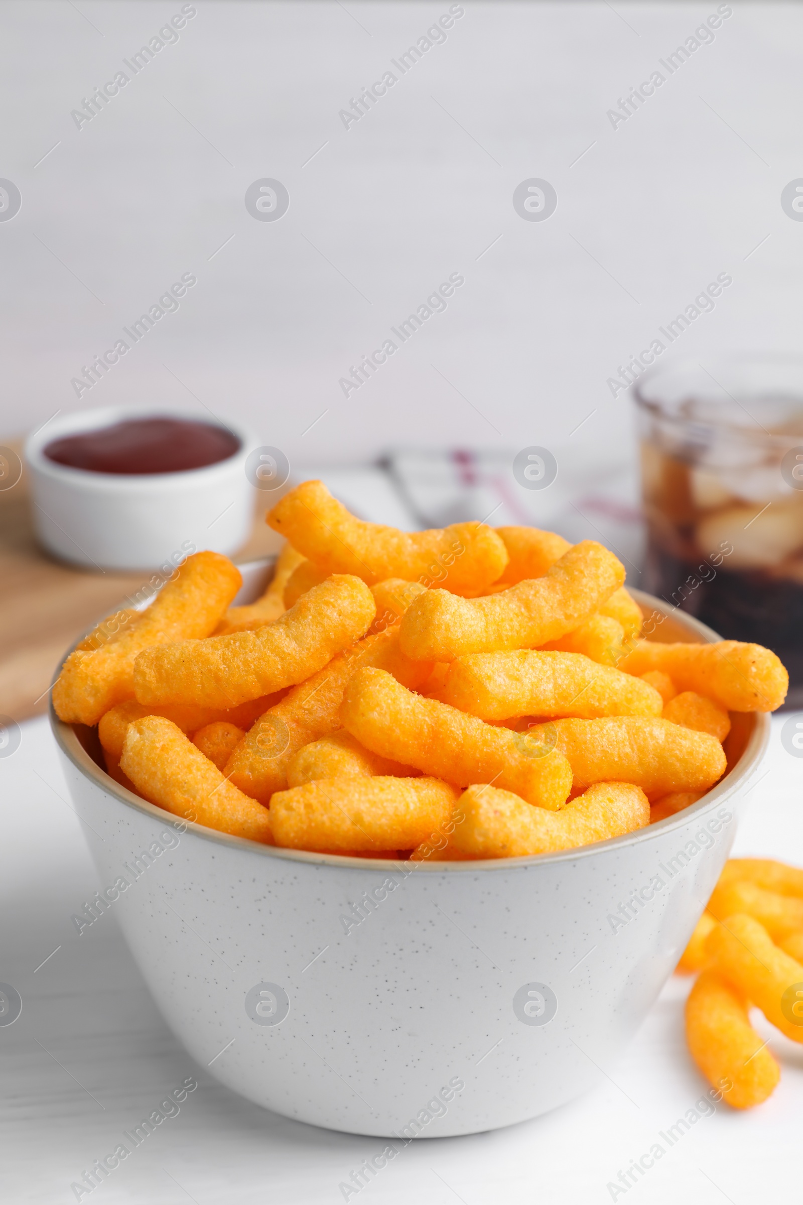 Photo of Crunchy cheesy corn snack in bowl on white wooden table, closeup