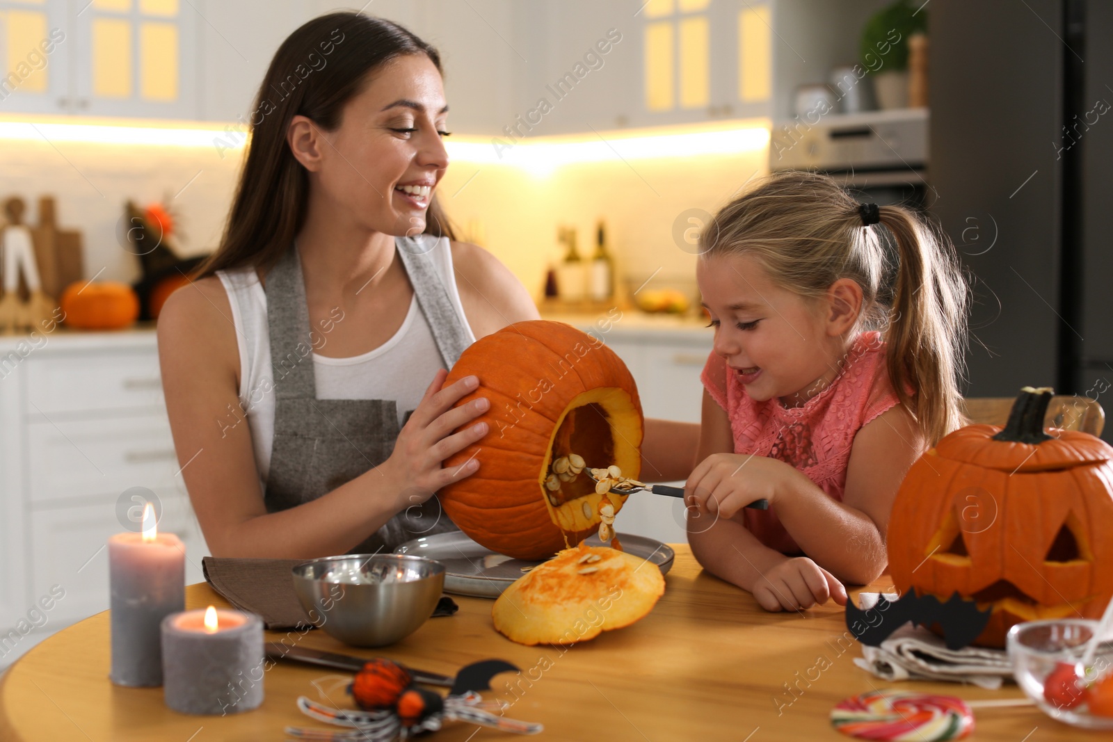 Photo of Mother and daughter making pumpkin jack o'lantern at table in kitchen. Halloween celebration