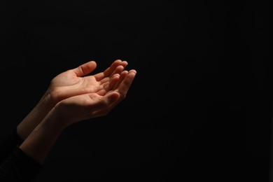 Photo of Religion. Woman with open palms praying on black background, closeup. Space for text