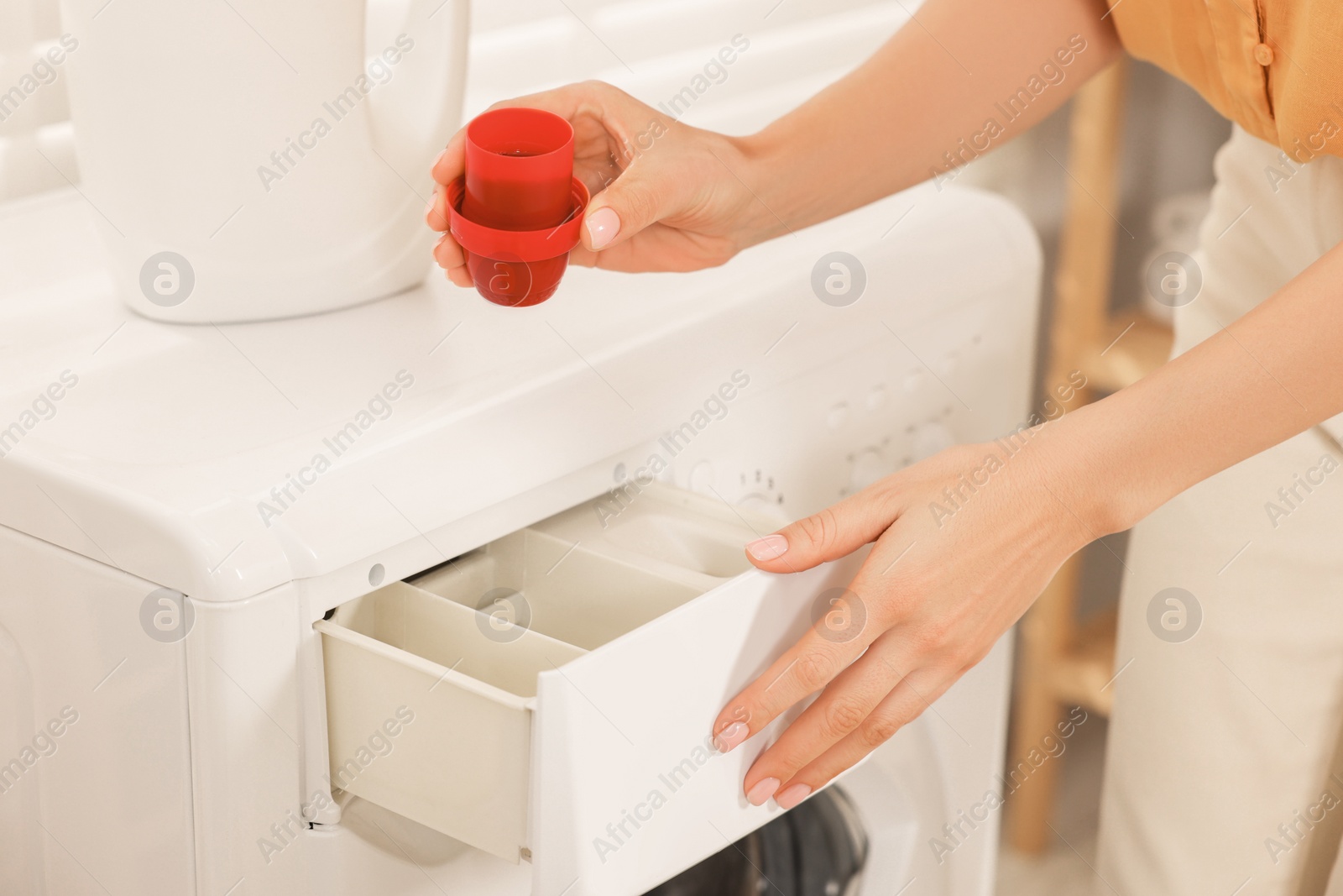 Photo of Woman with laundry detergent near washing machine indoors, closeup