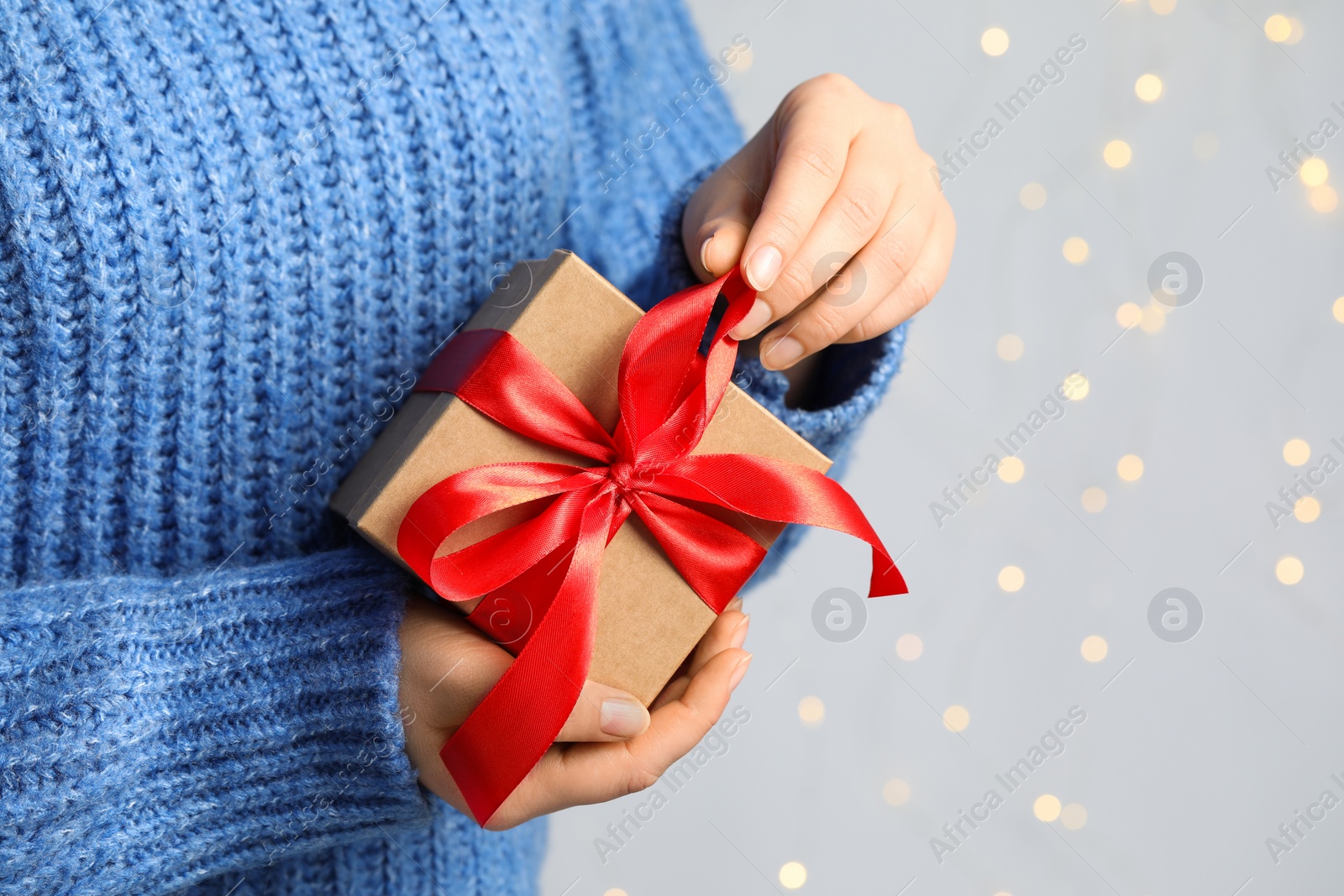 Photo of Woman holding gift box with red bow against blurred festive lights, closeup and space for text. Bokeh effect