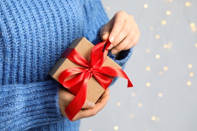 Woman holding gift box with red bow against blurred festive lights, closeup and space for text. Bokeh effect