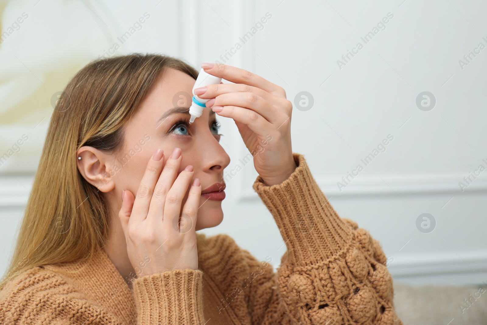 Photo of Young woman using eye drops at home