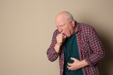 Photo of Senior man suffering from cough on color background. Space for text