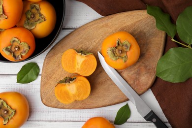 Photo of Whole and cut delicious ripe persimmons on white wooden table, flat lay