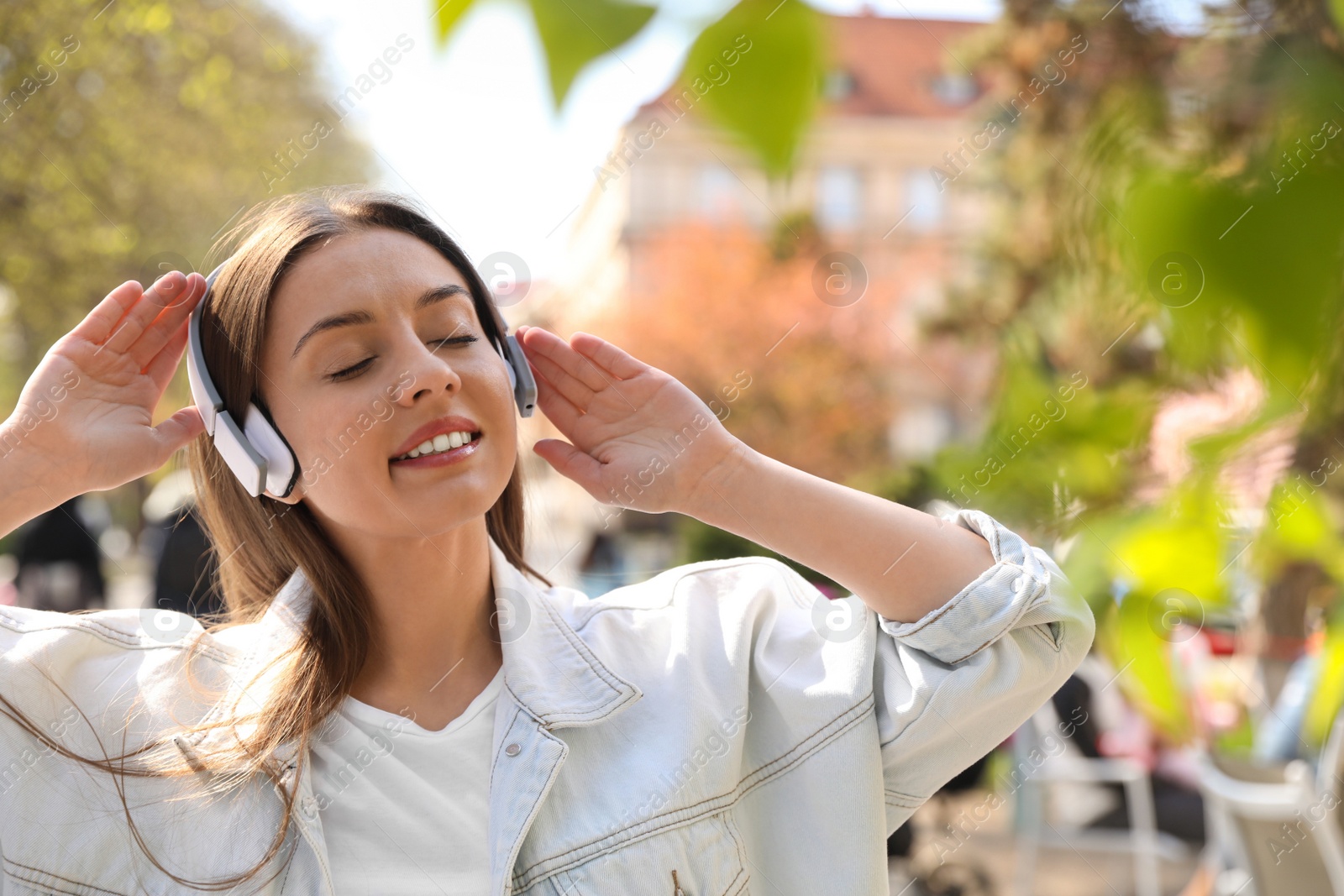 Photo of Young woman with headphones listening to music outdoors, space for text