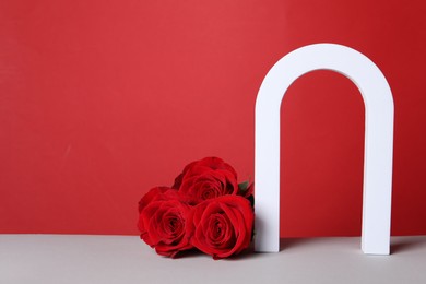Photo of Stylish presentation for product. Beautiful roses and geometric figure on white table against red background, space for text