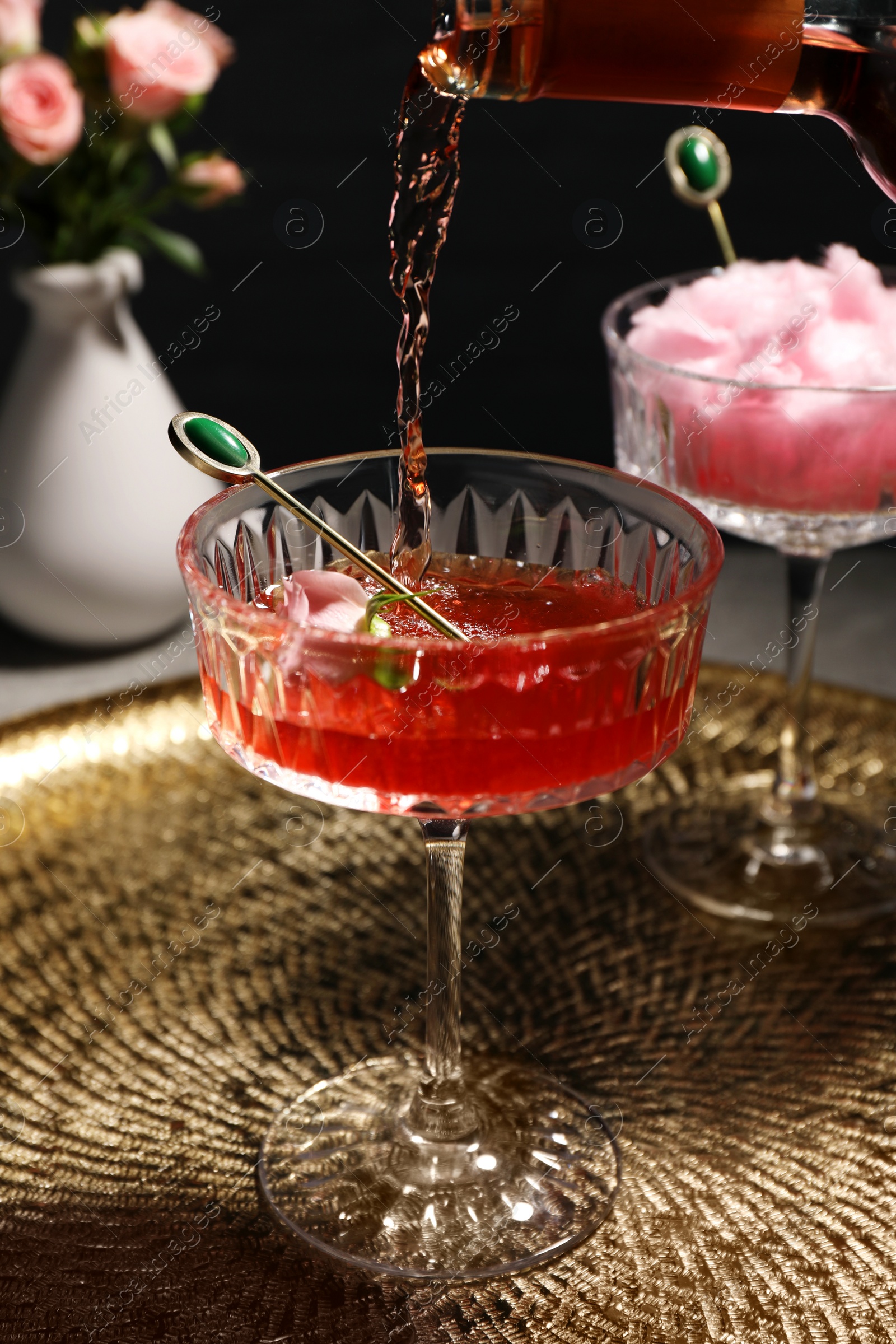 Photo of Pouring rose wine from bottle into glass on golden tray