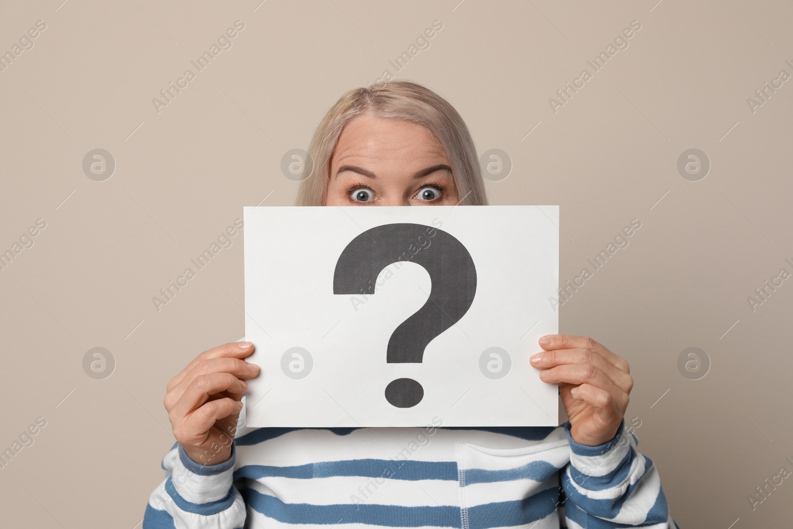 Photo of Mature woman holding paper with question mark on beige background