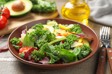 Photo of Tasty fresh kale salad on wooden table, closeup