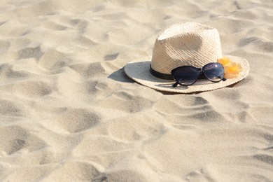 Photo of Hat with beautiful sunglasses and flowers on sand. Space for text